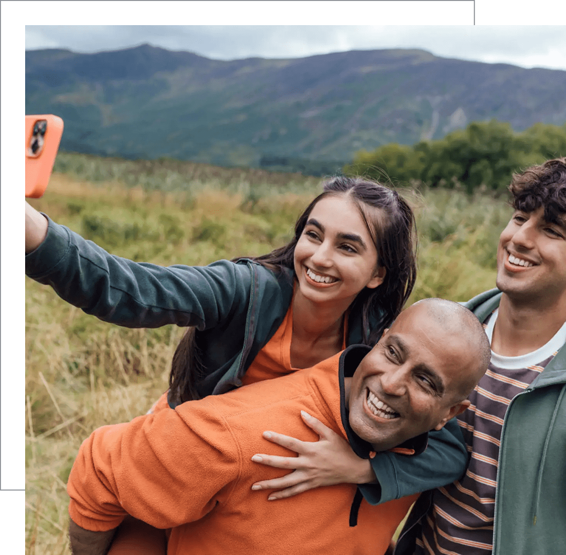Three friends taking a cheerful selfie outdoors with mountains in the background.