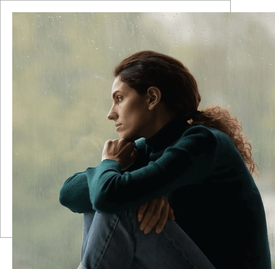 A woman with red hair sitting pensively by a window.