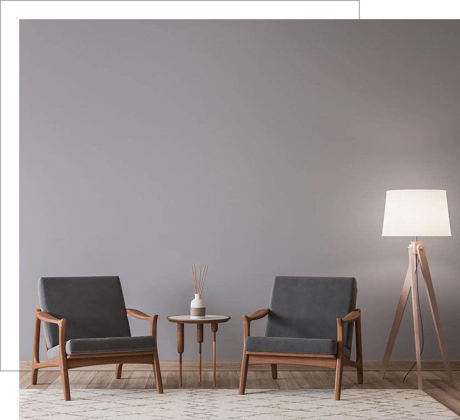 Two wooden armchairs with gray cushions and a small round table between them in a minimalist room.