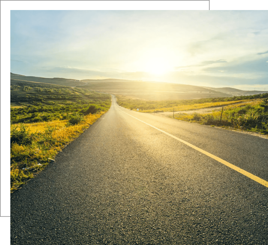 Open road leading to a bright sunrise over rolling hills.