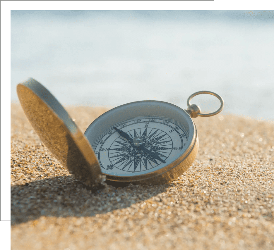 An open compass resting on sandy beach near water.